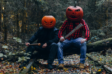 Two figures with pumpkin heads sit on a fallen tree in a dark forest during autumn nights