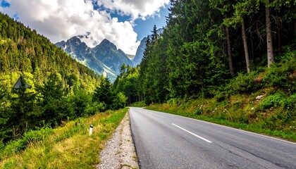 Fototapeta premium Asphalt road curves along vibrant green forest, leading towards majestic mountains under a partly cloudy sky. The path is a scenic view