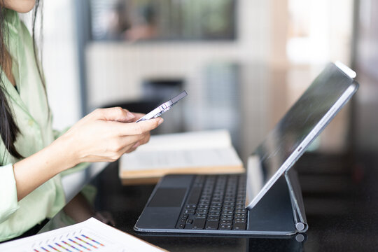 A woman is sitting at a desk with a laptop and a cell phone