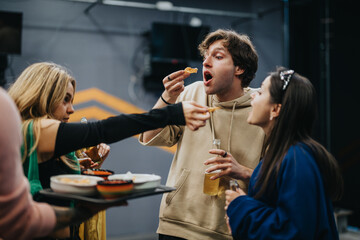 A cheerful group of friends socializing, sharing snacks, and having beverages in a relaxed indoor setting. A moment filled with laughter, bonding, and casual enjoyment of food and conversations.