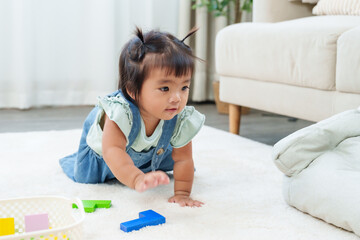 Sweet asian toddler girl crawling on carpet reaching colorful toy block eagerly developing movement coordination and curiosity representing early playful childhood exploration