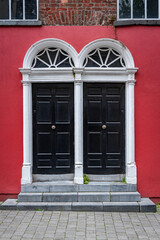 A typical wooden door in Ireland. Black doors on a residential building with a brick facade. Twin door.