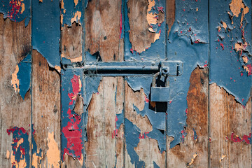 Vintage rusty deadbolt with padlock on the old wooden door. Horizontal closeup.  Cracked paint in several layers.