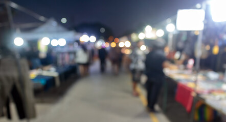 A blurry image of a bustling local evening market lined with glowing stalls, bright merchandise and warm evening light.