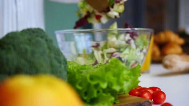 Woman's hands mixing a fresh vegetarian salad in a glass bowl with wooden spoons. Delicious and healthy food prepared with organic ingredients in a bright and cozy home kitchen
