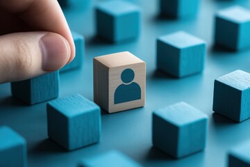 Choosing the Right Piece: A hand carefully selects a wooden block, featuring a person icon, from a field of blue blocks, symbolizing the selection or recruitment of individual