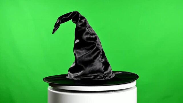 Black satin witch hat on a white pedestal against a vibrant green screen background for easy compositing and creative editing in fantasy and Halloween projects