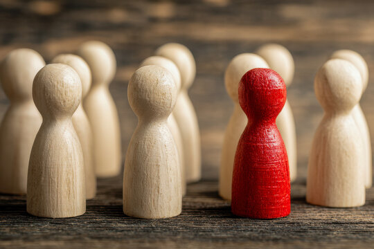 Wooden figurine painted red standing out prominently among a group of natural wooden figures symbolizing uniqueness and leadership in a rustic setting