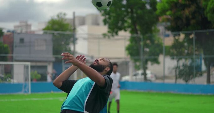 African American man doing headers on soccer field during practice, controlling ball with precision and focus in urban outdoor environment
