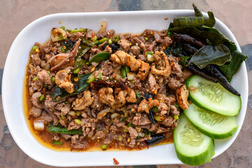 Spicy minced meat salad (Larb) with herbs, crispy pork, and cucumber on a white plate.