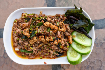 Spicy minced meat salad (Larb) with herbs, crispy pork, and cucumber on a white plate.