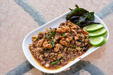 Spicy minced meat salad (Larb) with herbs, crispy pork, and cucumber on a white plate.