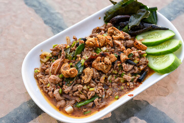 Spicy minced meat salad (Larb) with herbs, crispy pork, and cucumber on a white plate.