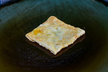 An egg crepe is cooked on a hot griddle, being folded with a spatula and tongs.