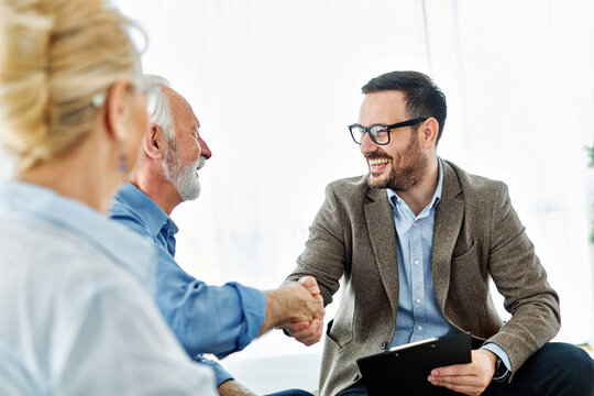 Portrait of a businessman or real estate agent or doctor shaking hands and signing a deal contract with senior couple in his office