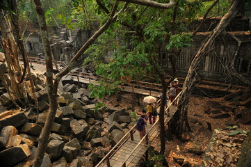 A few foreign tourists walking on wooden walkway at ruins of Beng Mealea Temple in Cambodia. 