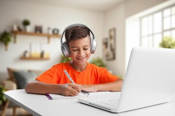 Happy small schoolboy does homework at room