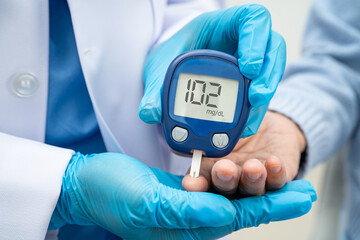 Asian doctor using digital glucose meter for check sample blood sugar level to treatment diabetes.