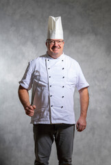 freundlicher Koch in Arbeitskleidung mit großem Rührbesen, Studioaufnahme.