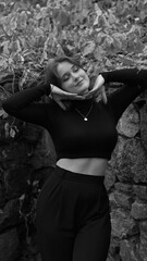 A woman in a black crop top and wide-leg pants stands by a stone wall on the steps in a park. She has her head thrown back and is relaxedly breathing in the fresh air, enjoying a moment of peace.
