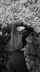 A woman in a black crop top and wide-leg pants stands by a stone wall on the steps in a park. She has her head thrown back and is relaxedly breathing in the fresh air, enjoying a moment of peace.