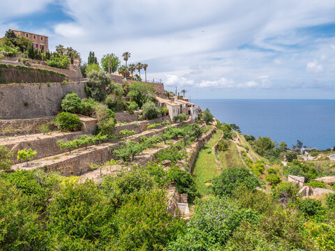 Banyalbufar, Mallorca. picturesque coastal village with terraced gardens and historic buildings sits on a hillside, overlooking the sea under a partly cloudy sky, Majorca
