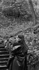 A woman in a black crop top and wide-leg pants stands by a stone wall on the steps in a park. She has her head thrown back and is relaxedly breathing in the fresh air, enjoying a moment of peace.