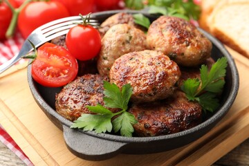 Delicious patties with parsley, tomatoes in pan and fork on wooden table, closeup
