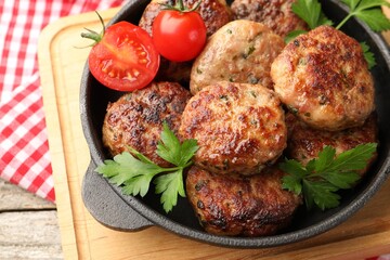 Delicious patties with parsley and tomatoes in pan on wooden table, above view