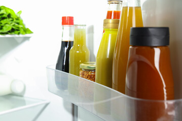 Bottles with different tasty sauces in fridge, closeup