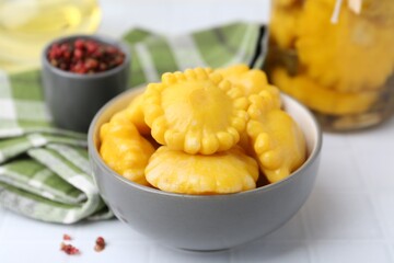 Pickled pattypan squashes in bowl on white tiled table, closeup