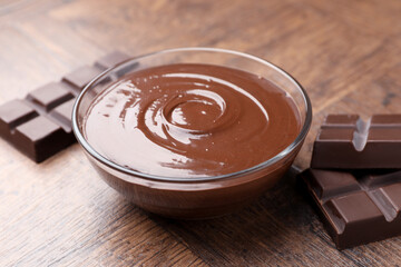 Bowl with melted chocolate and pieces on wooden table, closeup