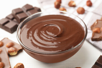 Melted chocolate and pieces with hazelnuts on white wooden table, closeup