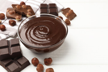Melted chocolate and pieces with hazelnuts on white wooden table, closeup. Space for text
