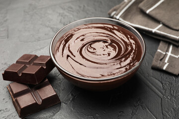 Bowl with melted chocolate and pieces on black table, closeup