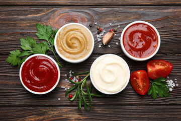 Different sauces, spices and herbs on wooden table, flat lay