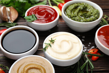 Different sauces, spices and herbs on wooden table, closeup
