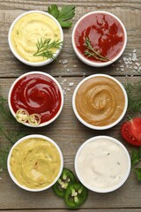 Different sauces and herbs on wooden table, flat lay