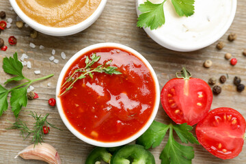 Different sauces, spices and parsley on wooden table, flat lay