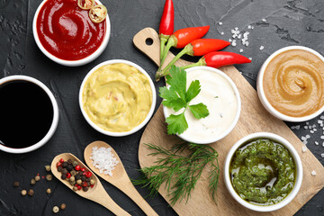 Different sauces, spices and herbs on black table, flat lay