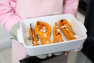 Woman with tasty baked pumpkin near oven indoors, closeup