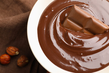 Melted chocolate with piece and hazelnuts on table, closeup