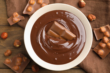 Melted chocolate and pieces with hazelnuts on wooden table, flat lay