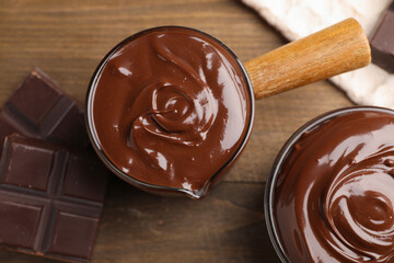 Melted chocolate and pieces on wooden table, flat lay