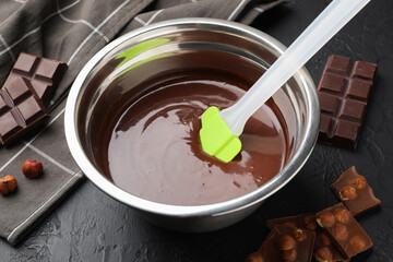 Melted chocolate and pieces with hazelnuts on black table, closeup