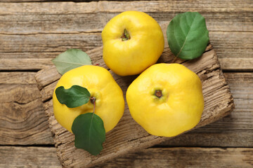 Fresh ripe quinces with leaves on wooden table, top view