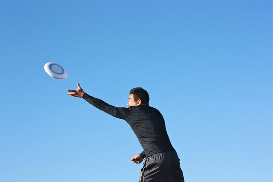 Side view of a man standing outdoors catching a frisbee in mid air