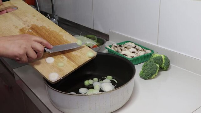 agregar ceboll&iacute;n picado en rodajas desde una tabla a una olla