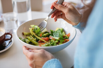 Close-up of a woman sitting at a table eating a healthy salmon salad with a glass of water and cappuccino