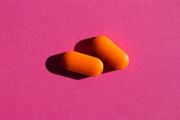 Two orange pills on pink background